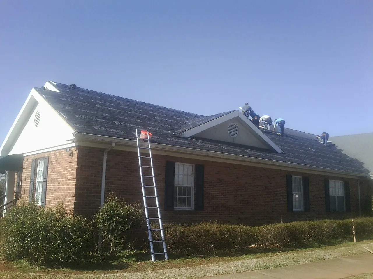 Crew tearing shingles off a brick ranch roof with a ladder set — Metal Roof Repair work by our crew in Enterprise