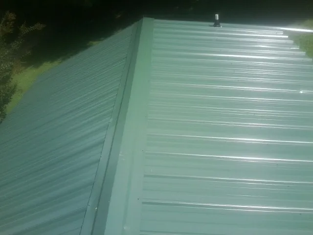 New green metal panels meeting at the ridge of a roof — Flat Roof Repair work by our crew in Enterprise