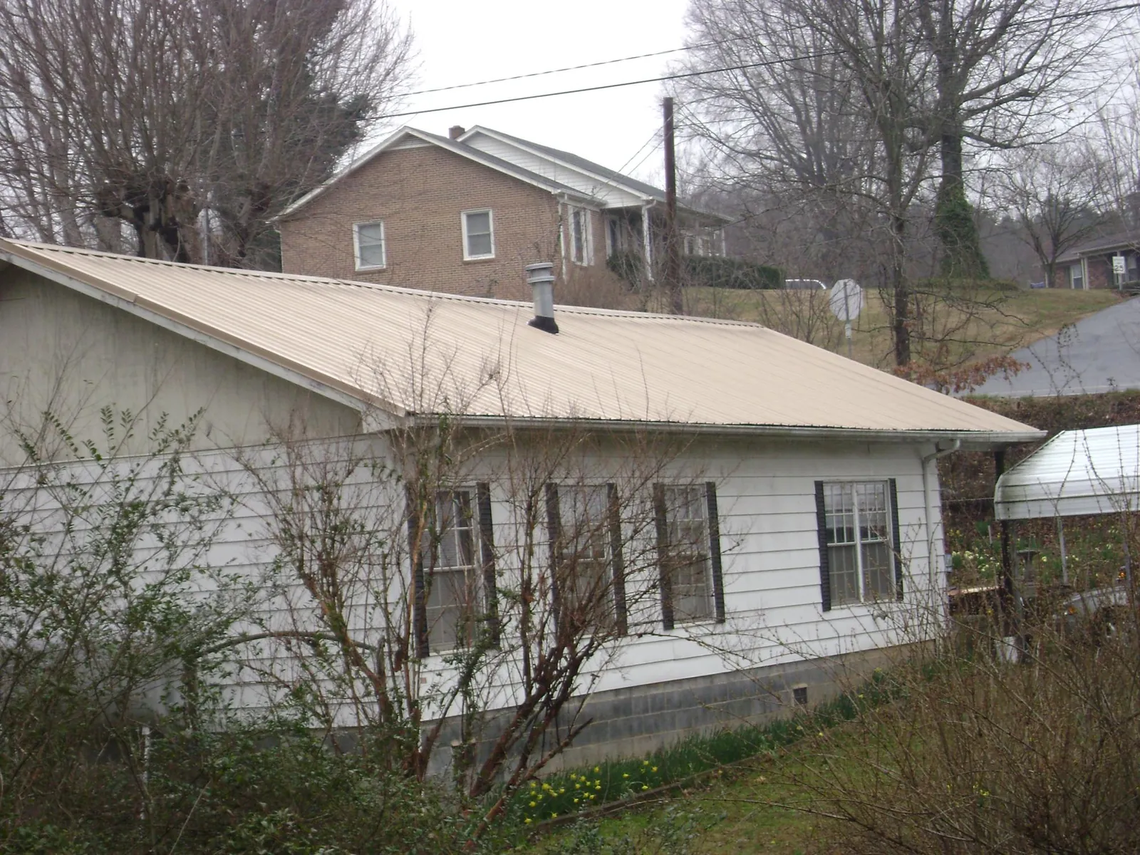 Tan metal roof on a white sided house set into a hillside — Commercial Roofing by Roofing Brothers in Enterprise